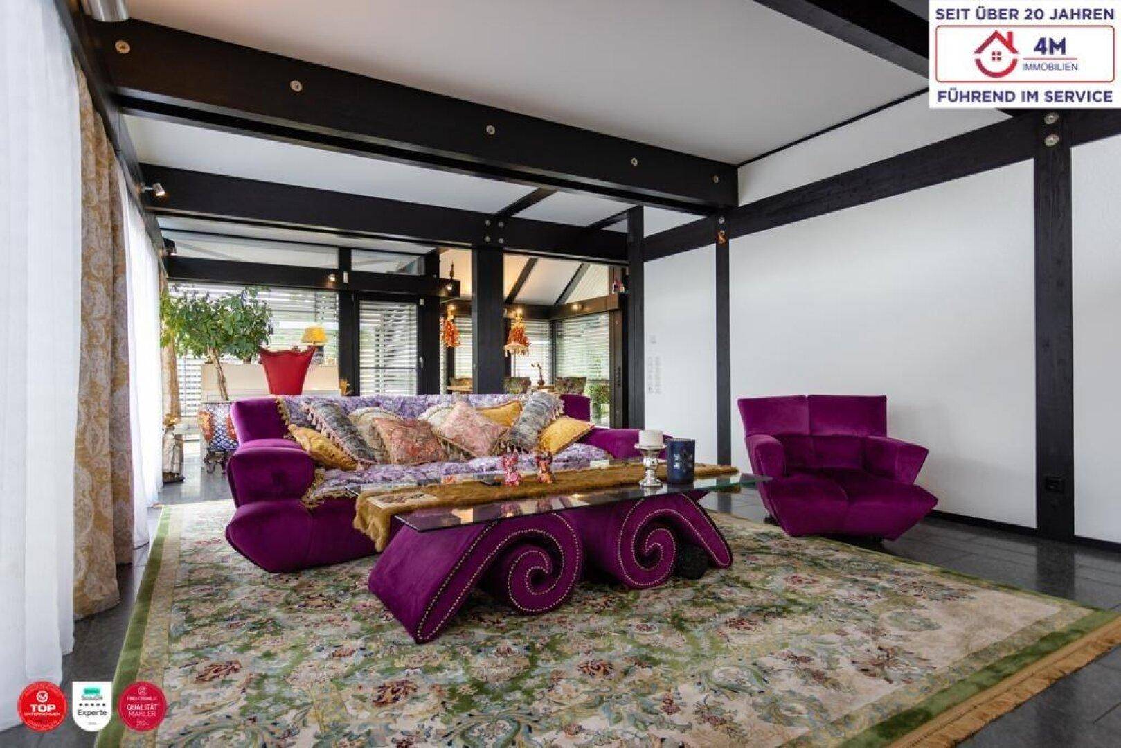 Geräumiges Wohnzimmer mit auffälligen violetten Möbeln, dunklen Holzbalken und einem gemusterten Teppich.