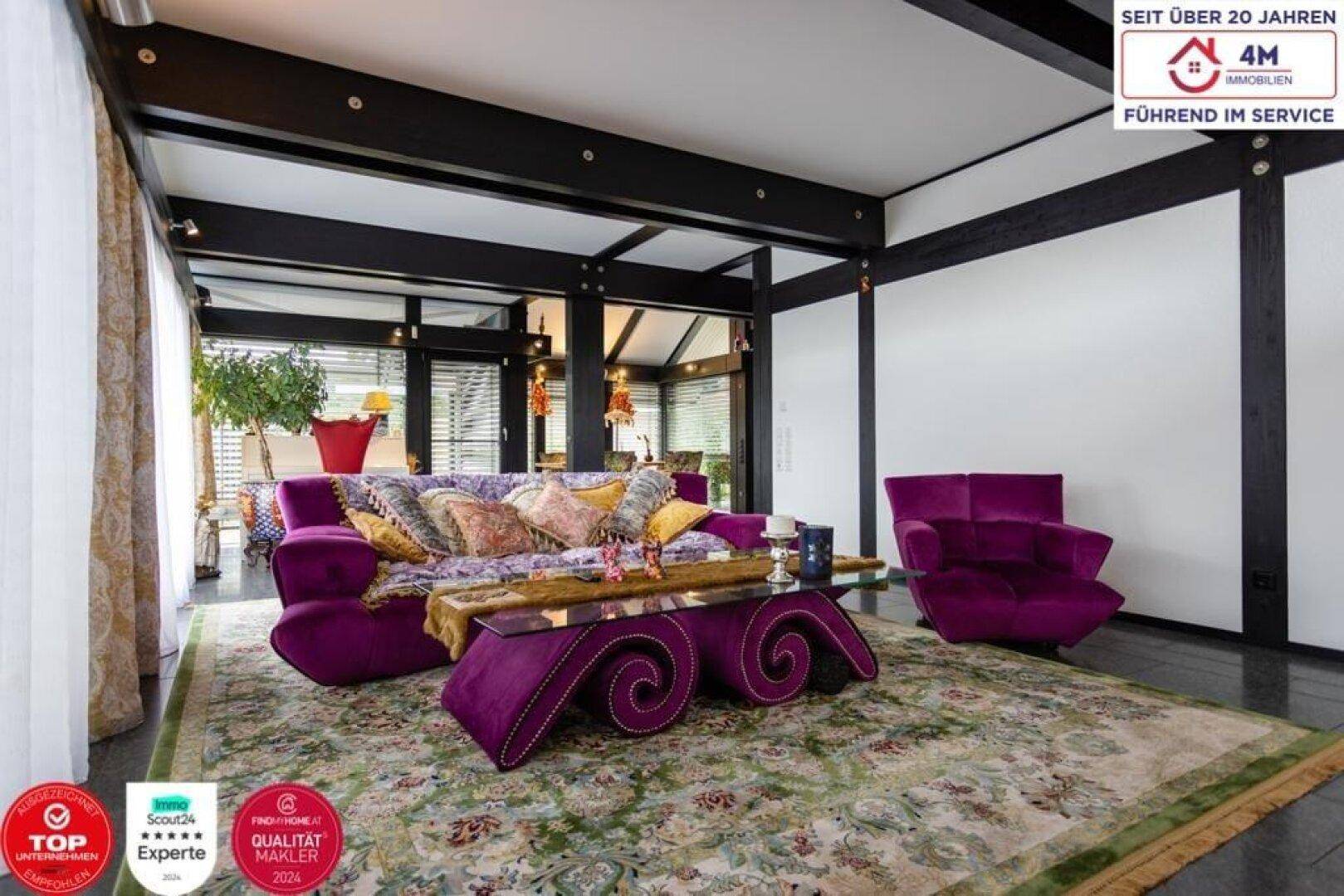 Gemütliches Wohnzimmer mit auffälligem lila Sofa, Teppich und großen Fenstern.