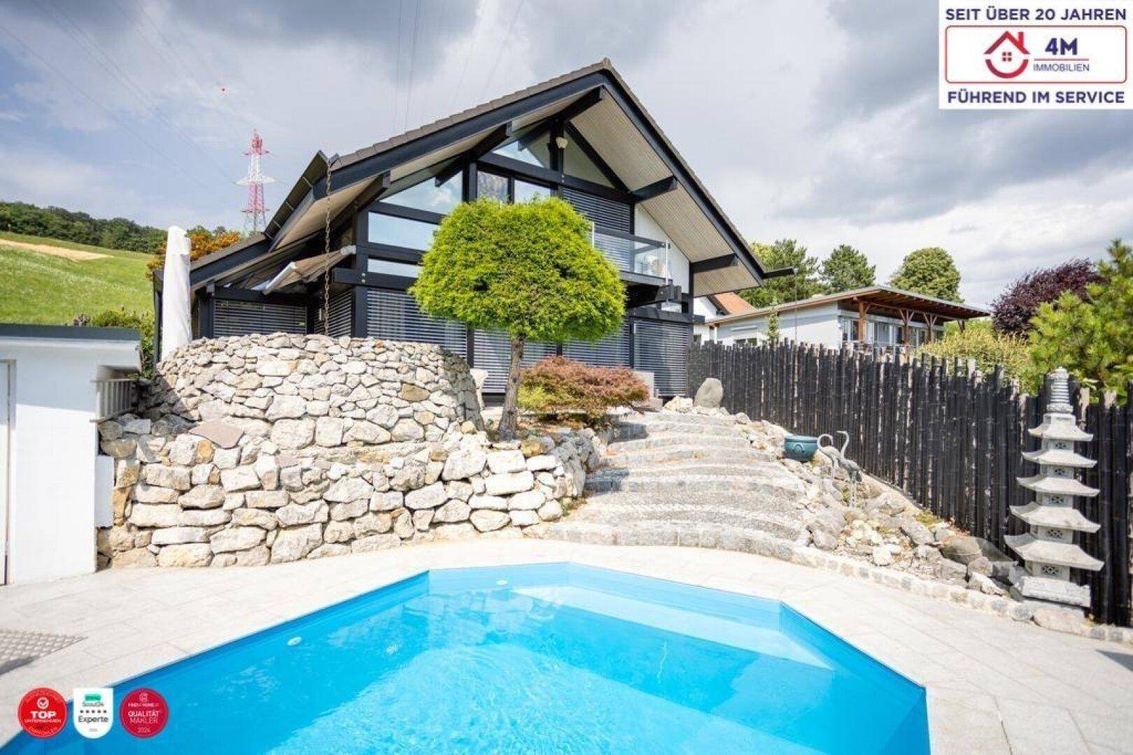 Modernes Haus mit Poolbereich und Steinterrassen, umgeben von grüner Landschaft.