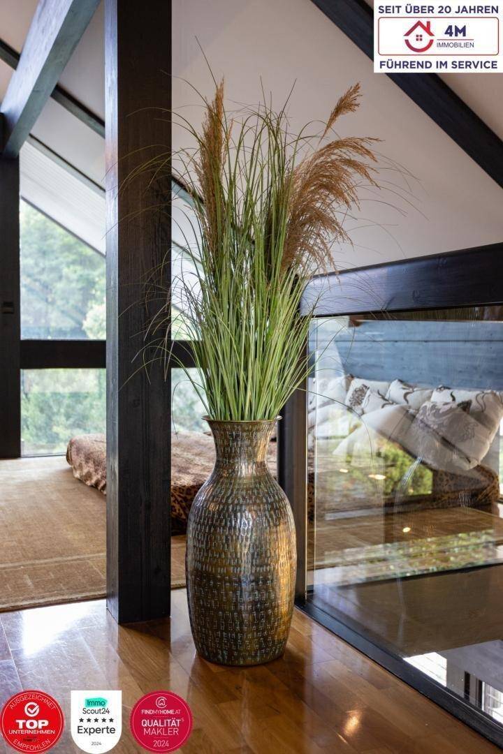 Dekorative Vase mit Pflanzen auf Holzfußboden, neben einer Glasbrüstung.