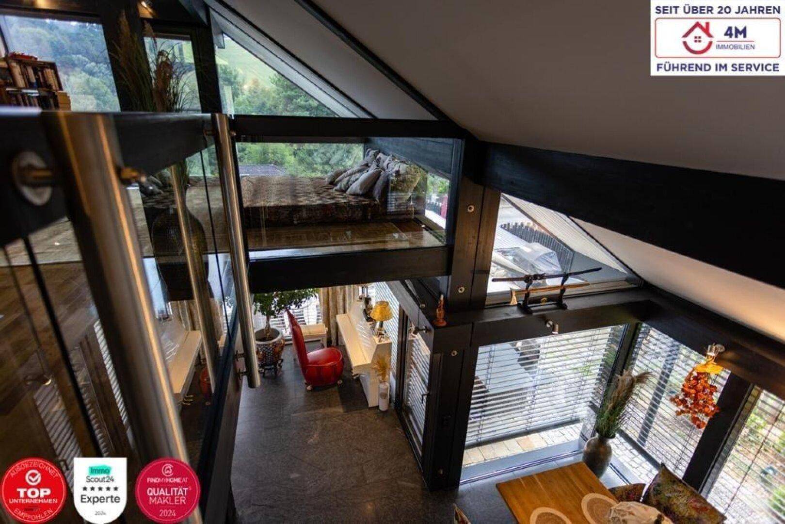 Offener Wohnbereich mit Blick auf ein Schlafzimmer im Obergeschoss und große Fenster.