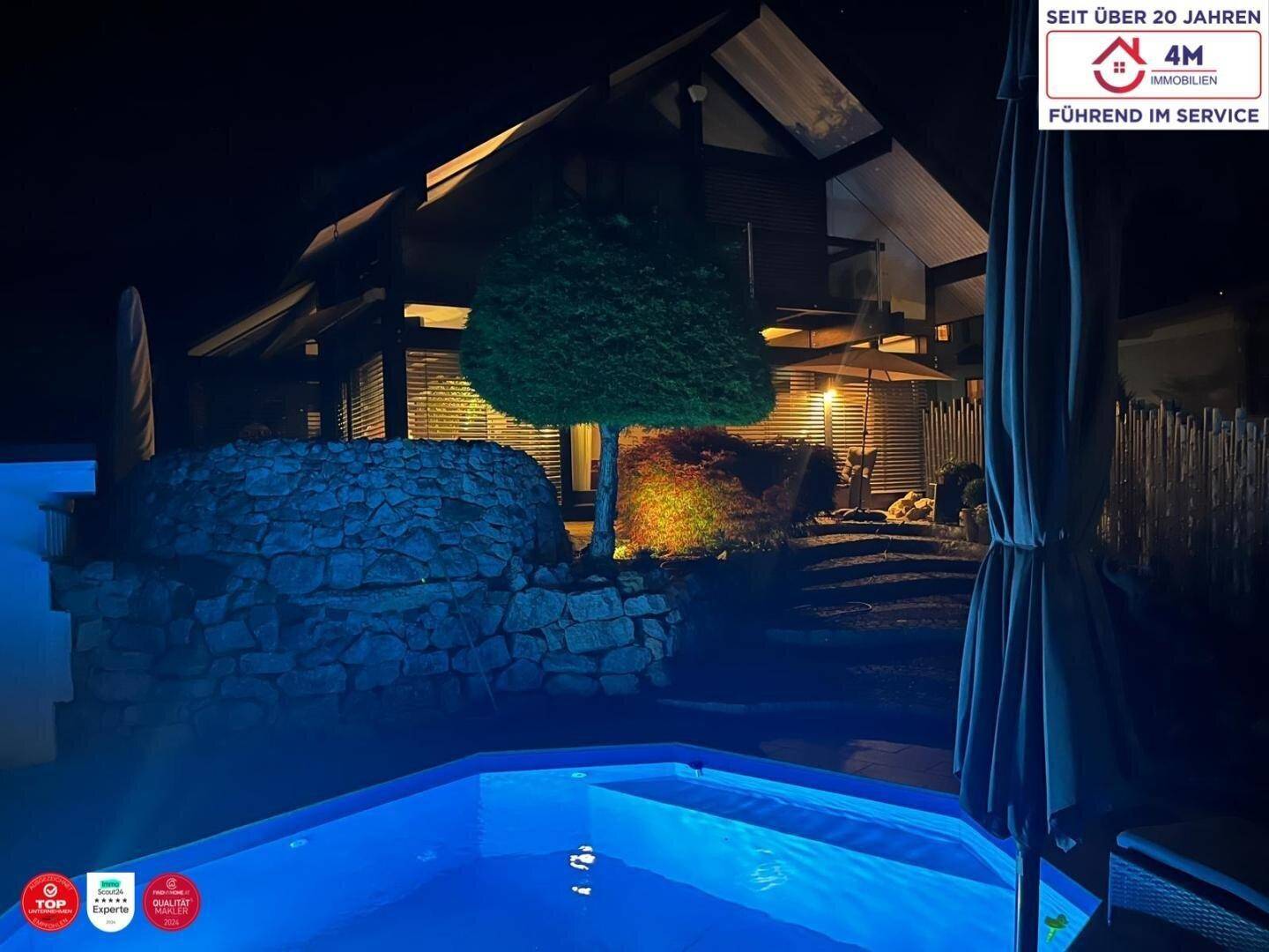 Außenbereich bei Nacht mit beleuchtetem Pool, umgeben von Steinmauern und der Architektur des Hauses.
