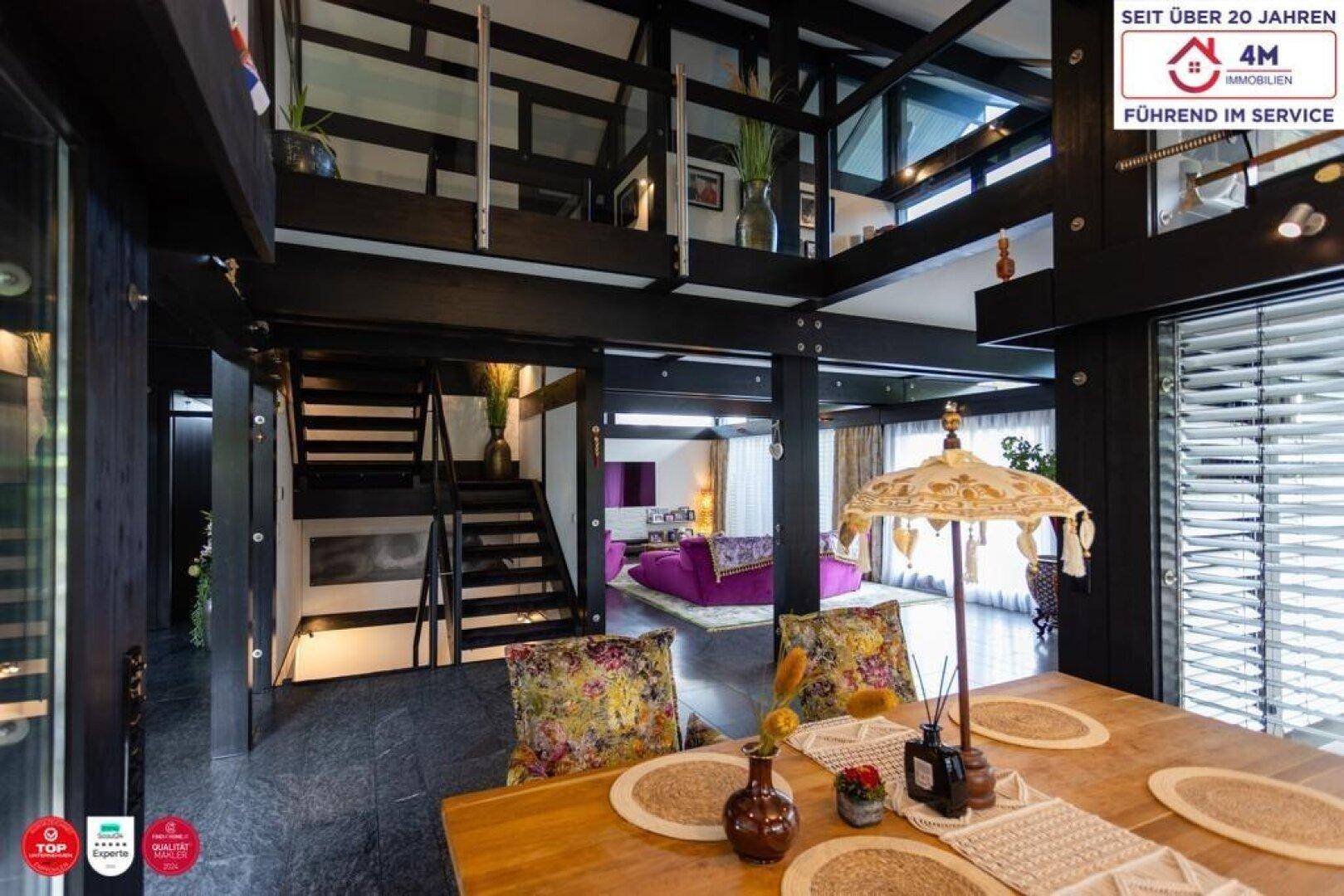 Geräumiger Wohn- und Essbereich mit dunklem Boden und offener Treppe.