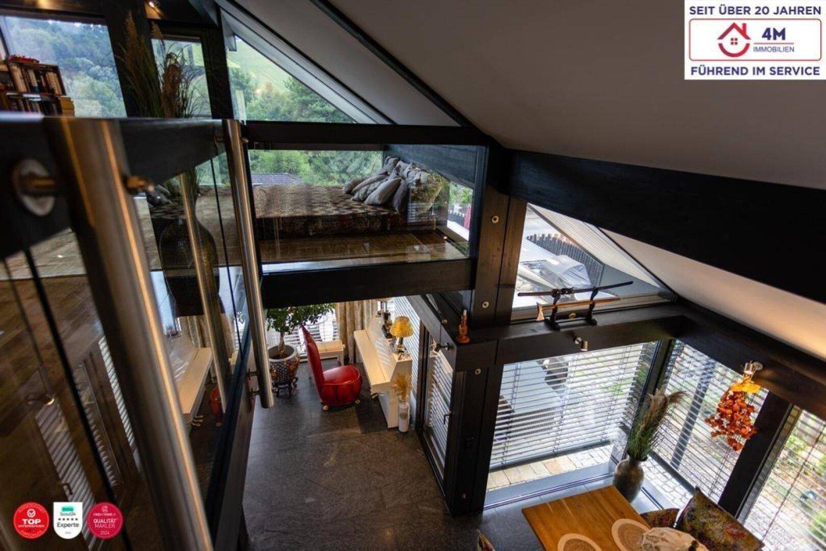 Offener Wohnbereich mit Blick auf ein Schlafzimmer im Obergeschoss und große Fenster.