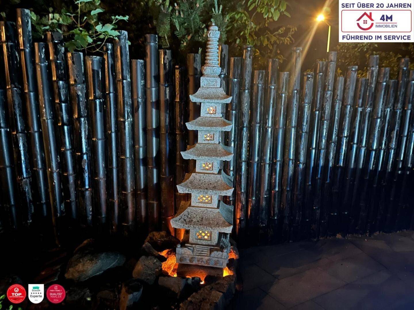 Japanischer Steinturm als Gartendekoration, umgeben von Bambuszaun und beleuchtet in der Nacht.