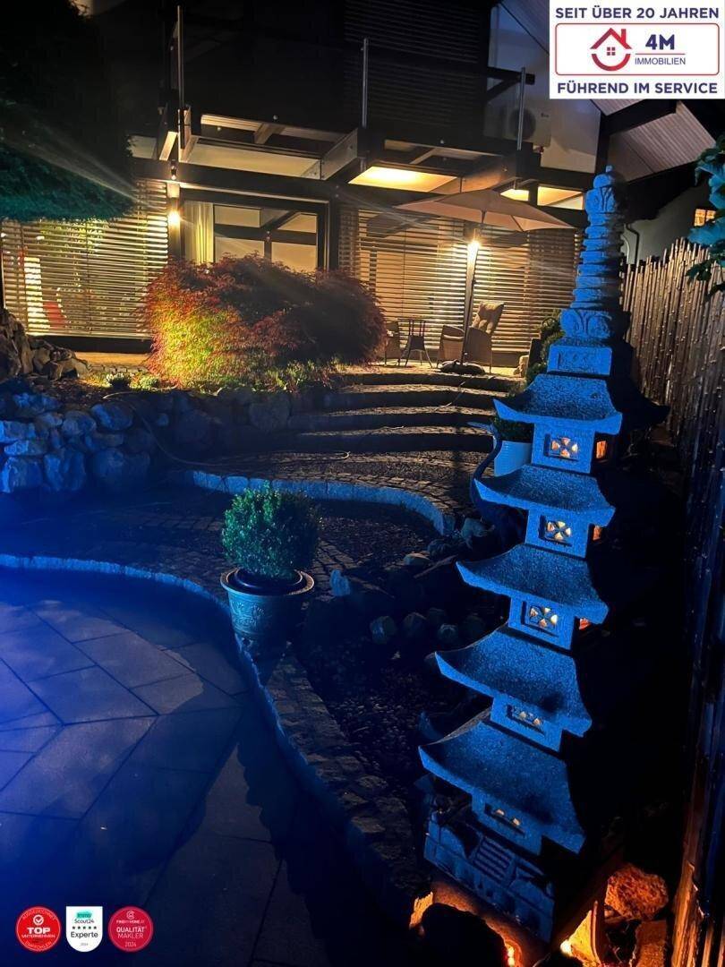 Nächtlicher Gartenbereich mit beleuchtetem Pool, japanischem Steinturm und üppiger Bepflanzung.