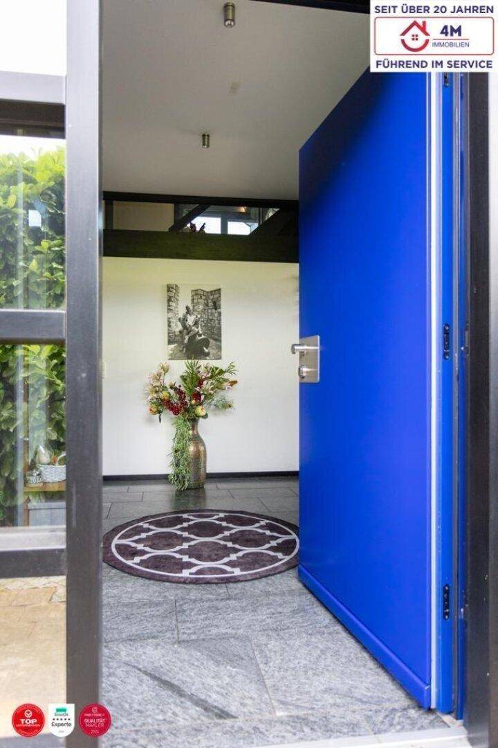 Heller Eingangsbereich mit einer auffälligen blauen Tür, Steinfliesenboden und einem Blumenarrangement.