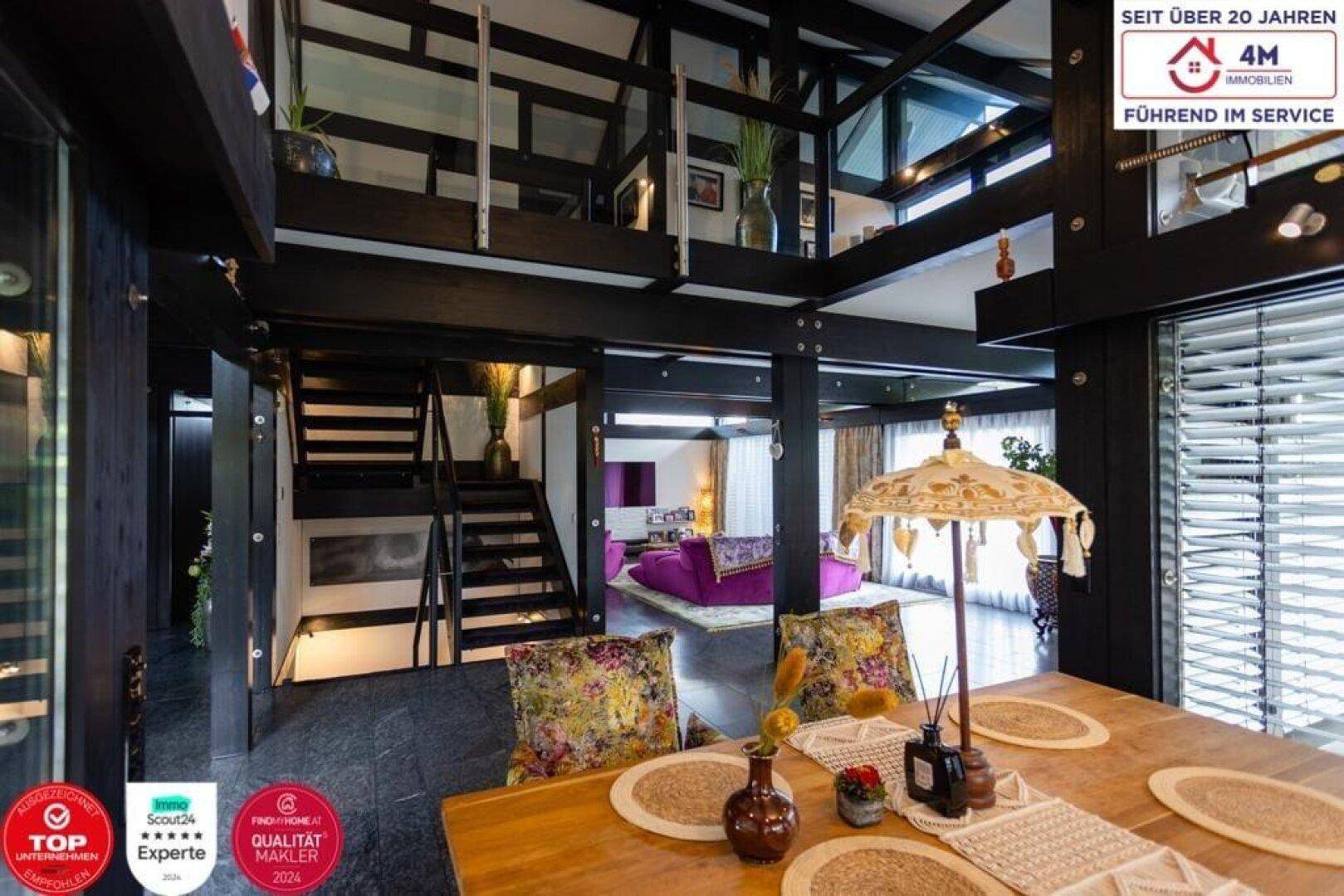Geräumiger Wohn- und Essbereich mit dunklem Boden und offener Treppe.