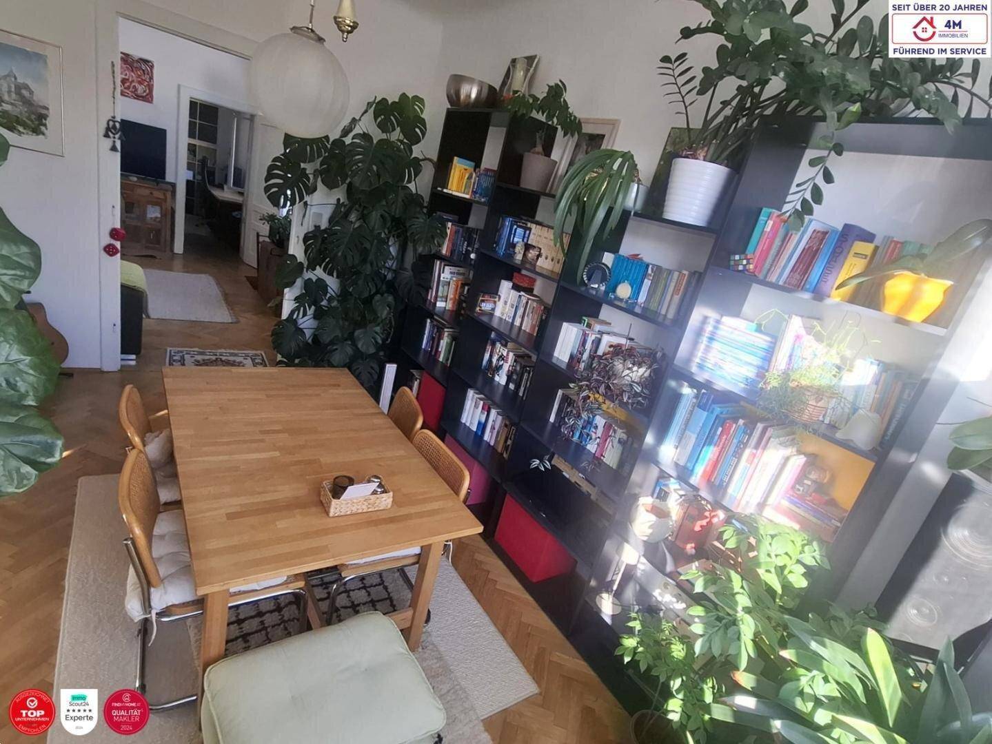 Gemütlicher Essbereich mit Holztisch, Bücherregalen und vielen Pflanzen, offen zum Wohnzimmer.