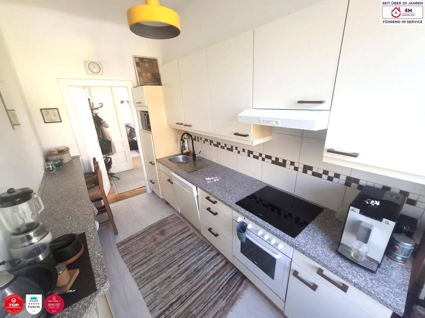 Funktionale Küche mit weißen Fronten, Induktionskochfeld, Backofen und Kaffeemaschine.