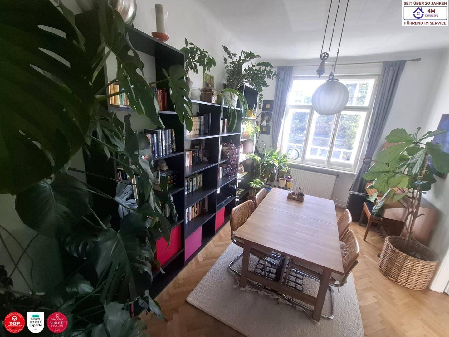 Heller Essbereich mit Holztisch, umgeben von Pflanzen und einem großen Fenster mit Blick ins Grüne.