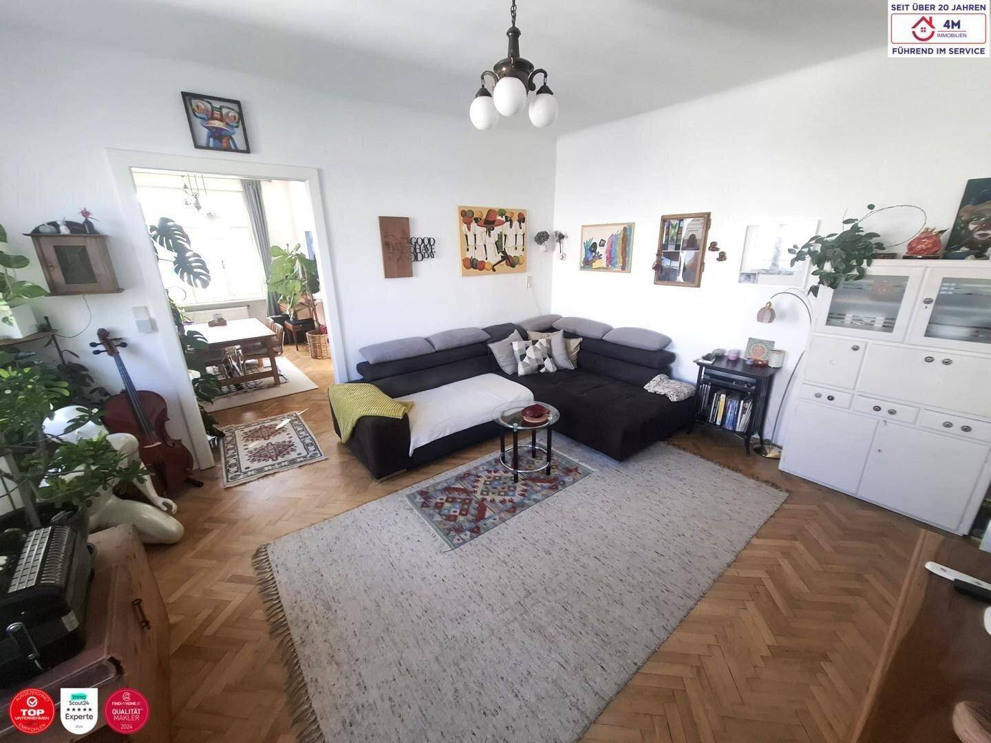 Geräumiges Wohnzimmer mit Ecksofa, Parkettboden und dekorativen Elementen, die zum Essbereich führen.