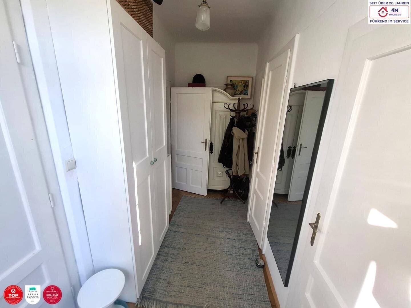 Schmaler Flur mit weißem Einbauschrank, Garderobe und Spiegel, der zum Wohnbereich führt.