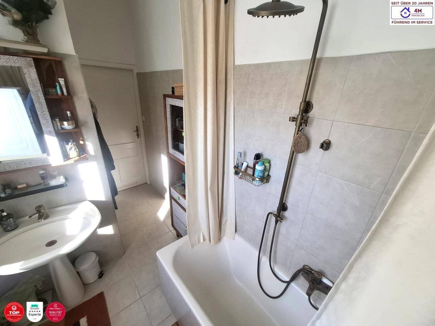 Badezimmer mit Badewanne, Duschvorhang und Waschbecken, hell beleuchtet.