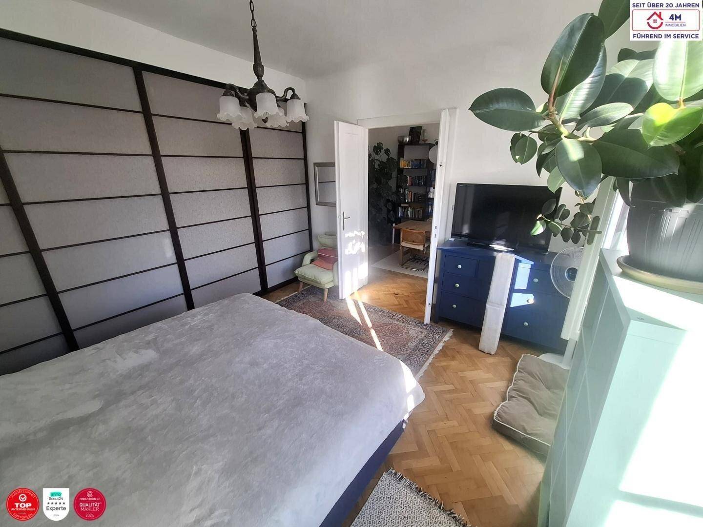 Helles Schlafzimmer mit Doppelbett, Parkettboden und Zugang zu einem weiteren Raum.