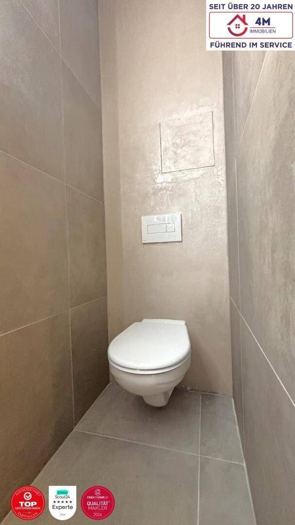 Separates WC mit Wand-WC und modernen grauen Fliesen, minimalistisch und funktional.