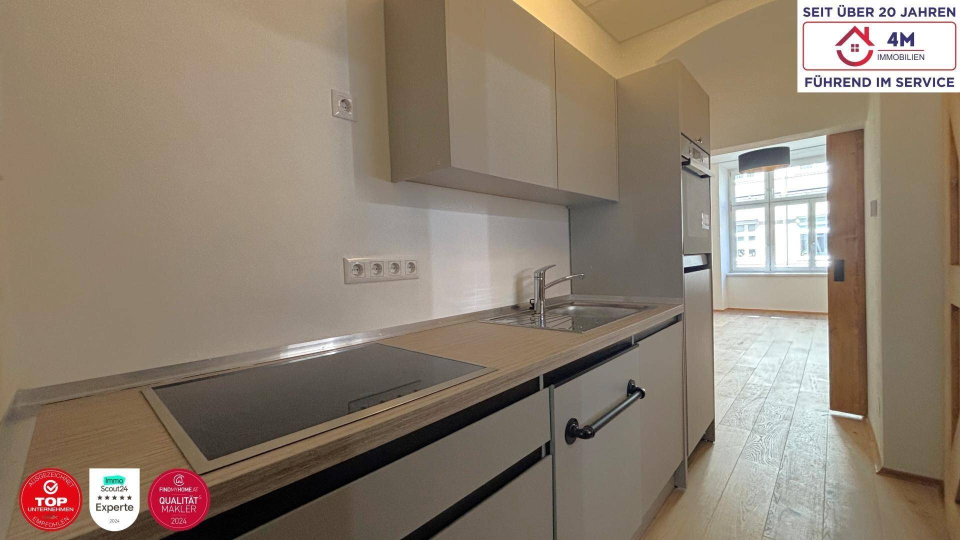 Moderne Küchenzeile mit integrierten Geräten und hellem Holz-Look, offen zum Wohnbereich.