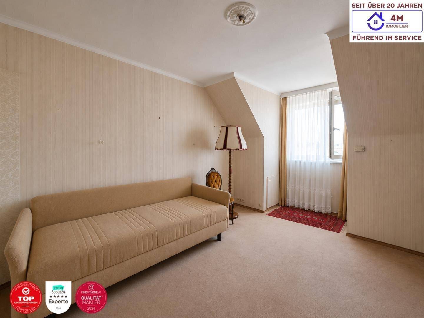 Gemütliches Wohnzimmer mit beigem Sofa, Stehlampe und Fenster unter einer Dachschräge.