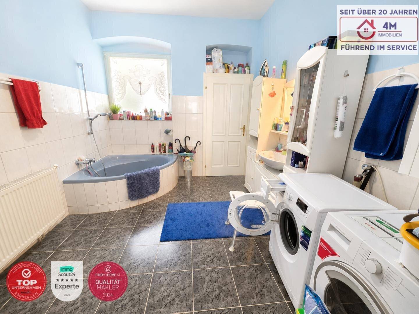 Geräumiges Badezimmer mit Eckbadewanne, Waschmaschine und Trockner sowie hellen Fliesen.