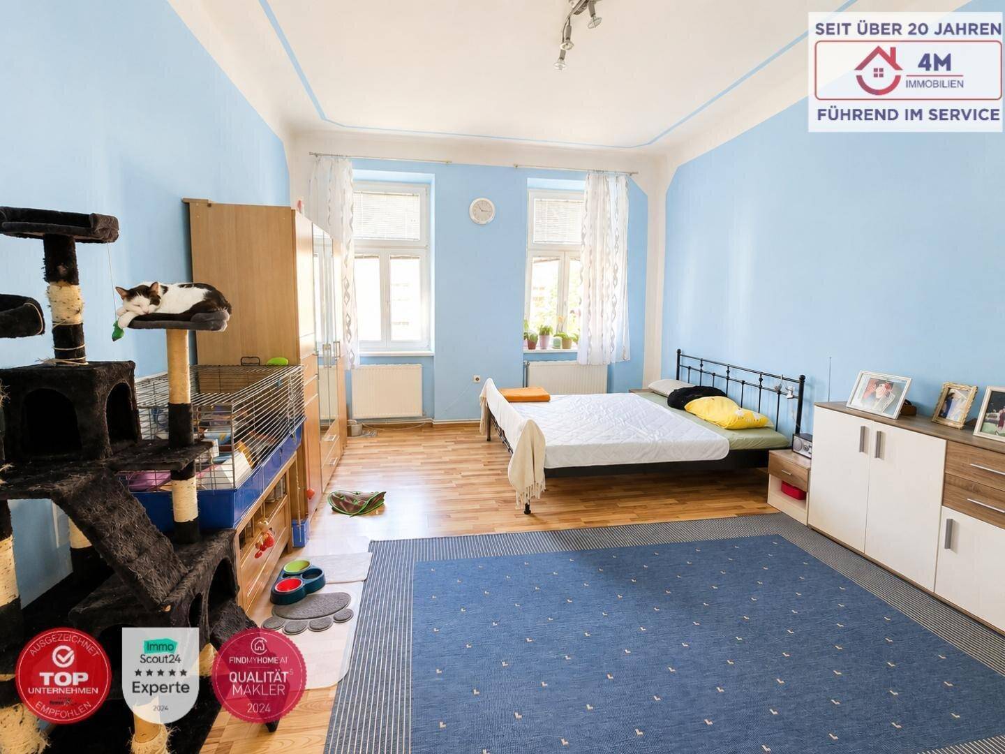 Helles Schlafzimmer mit Holzboden, Doppelbett und einem großen Teppich in Blautönen.
