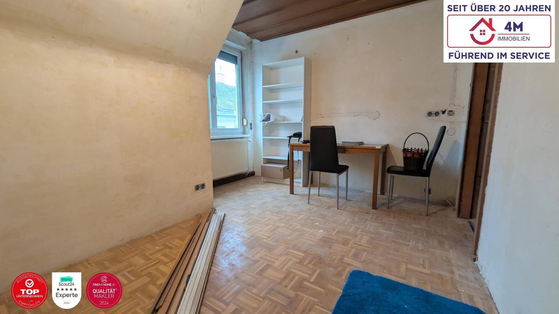 Unrenoviertes Zimmer mit Dachschräge, Parkettboden und einfacher Möblierung.