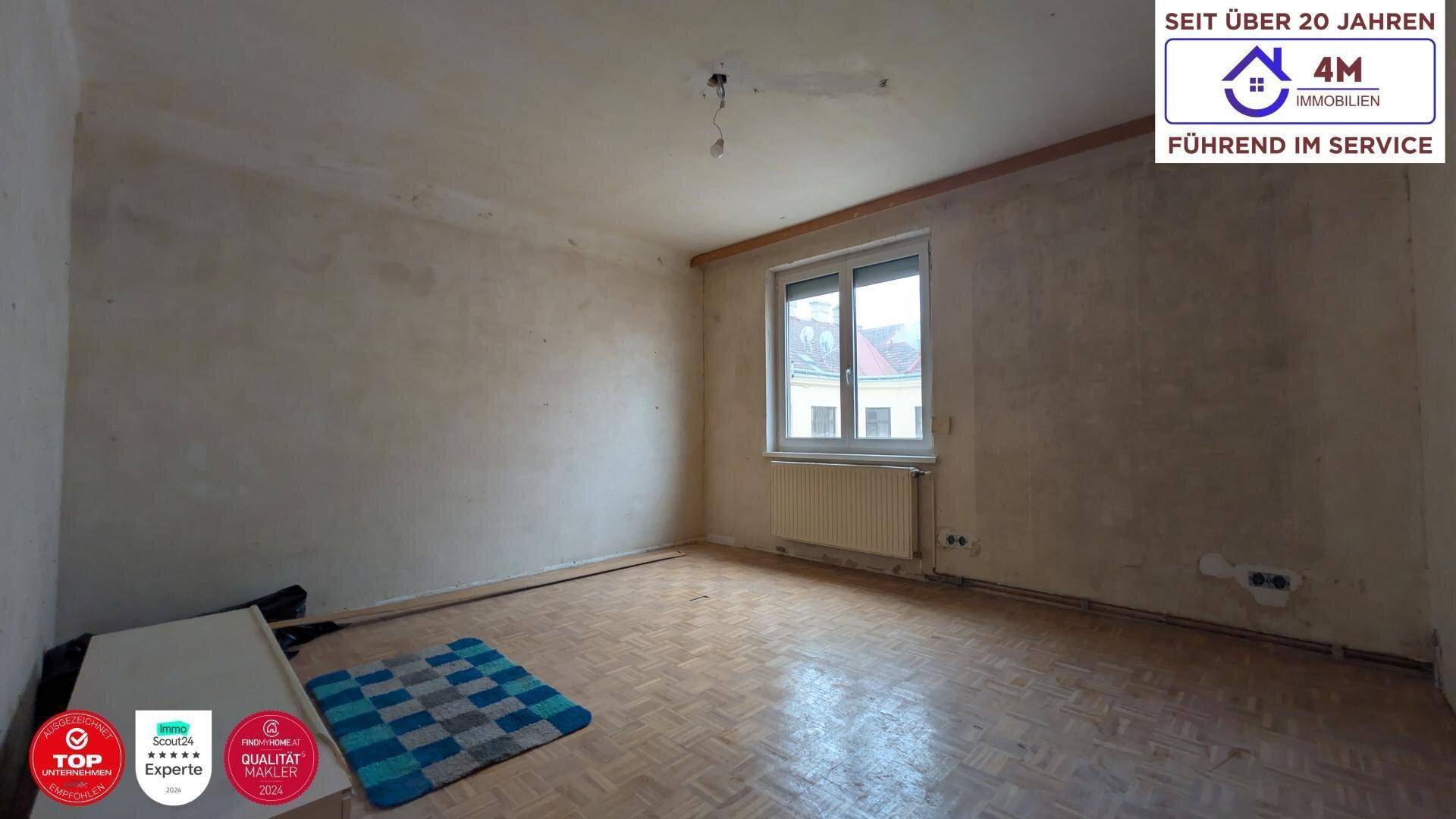 Unrenoviertes Zimmer mit Fenster, Heizkörper und Parkettboden.