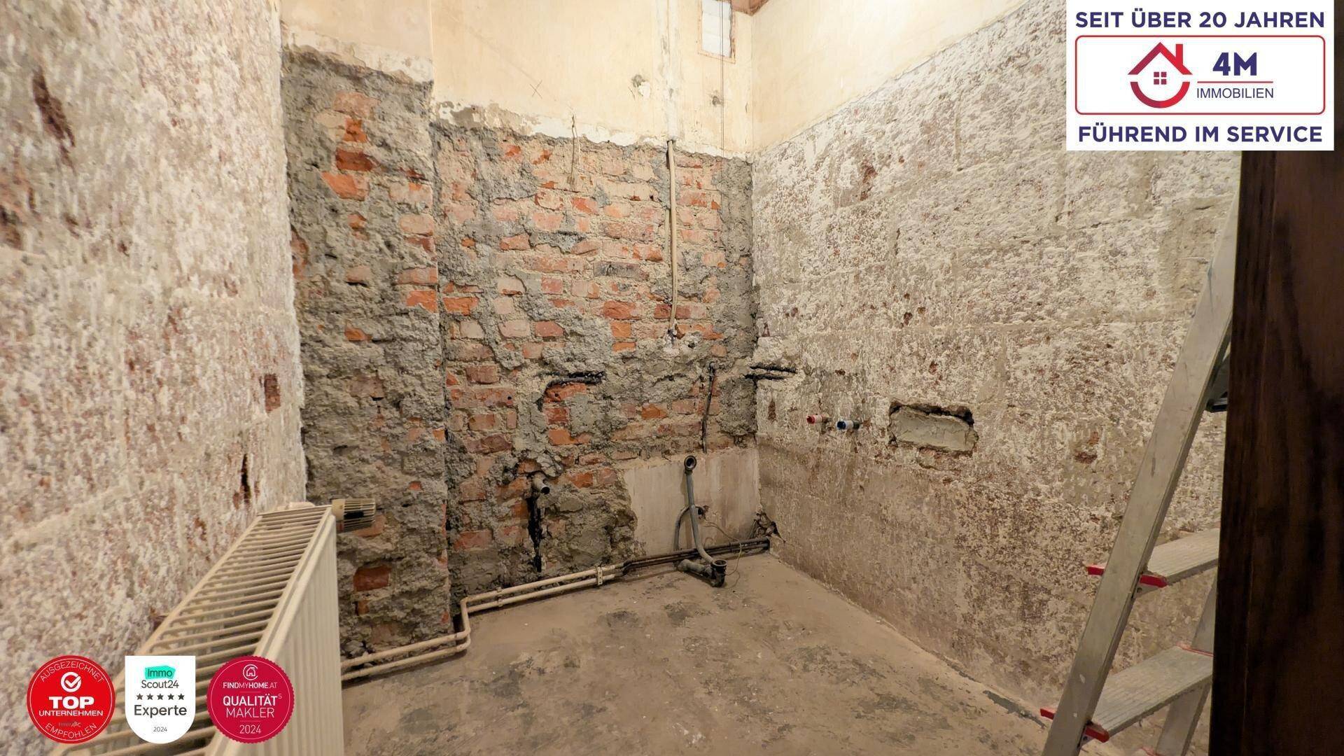 Badezimmer im Rohbauzustand mit freigelegten Ziegelwänden und Installationen.