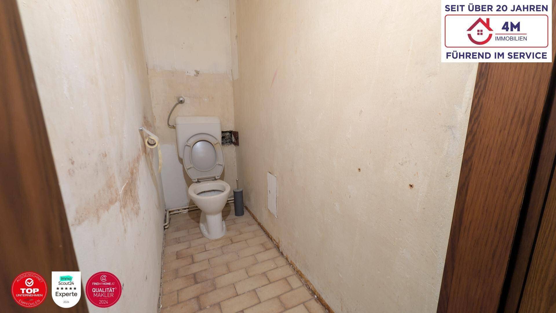 Einfaches Gäste-WC mit alter Toilette und Fliesenboden, renovierungsbedürftig.