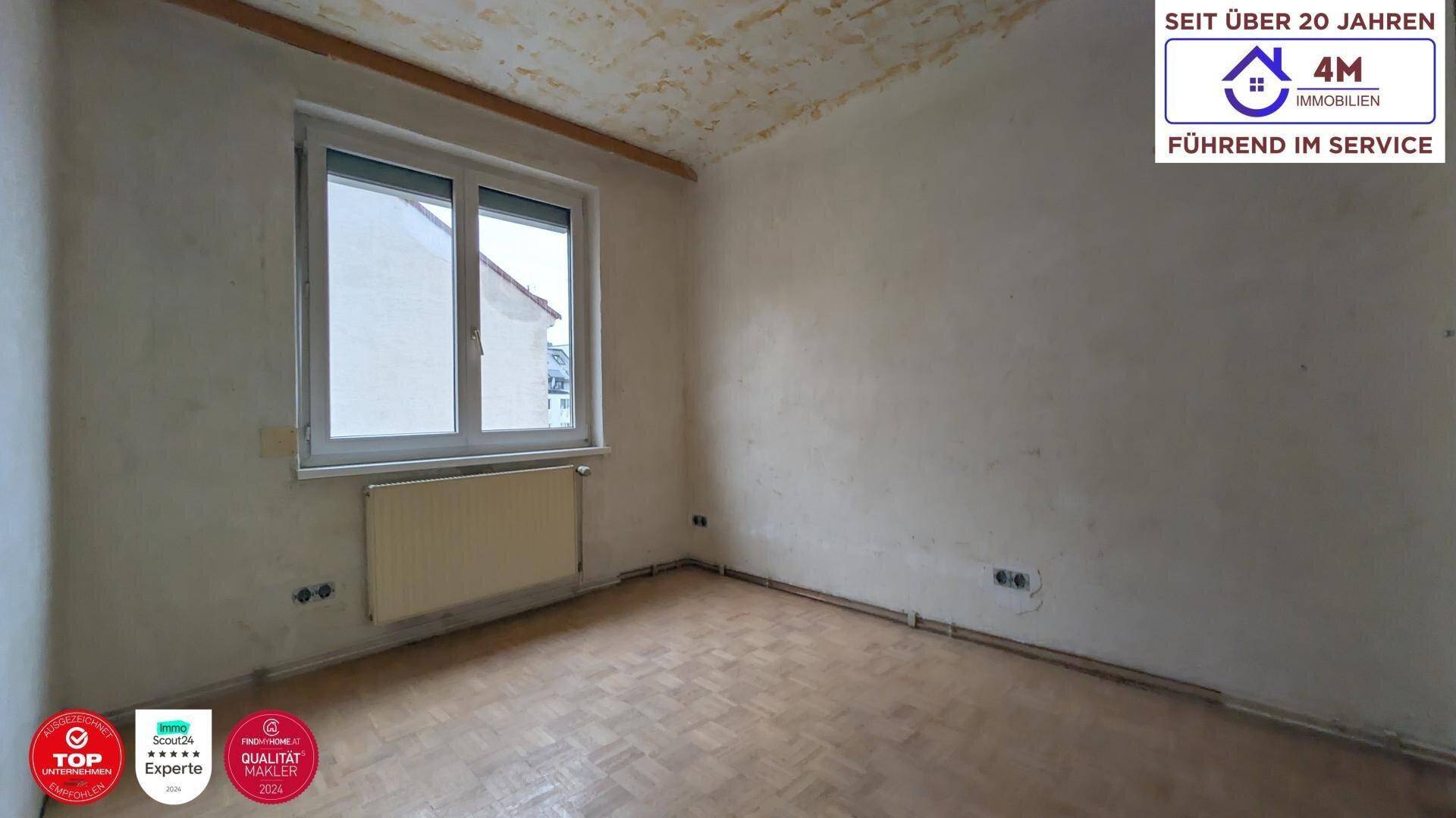 Unrenoviertes Schlafzimmer mit Fenster, Heizkörper und Parkettboden.