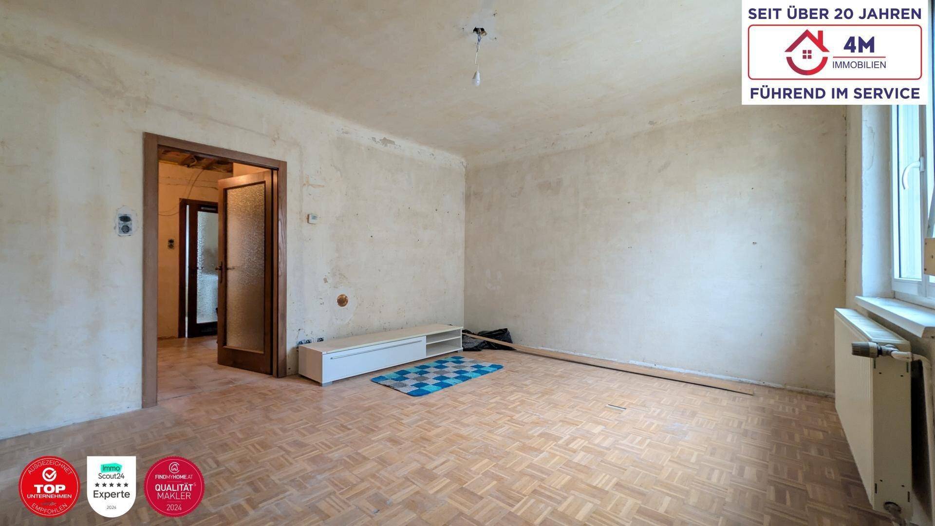 Unrenoviertes Wohnzimmer mit Parkettboden, Fenster und Renovierungsbedarf.