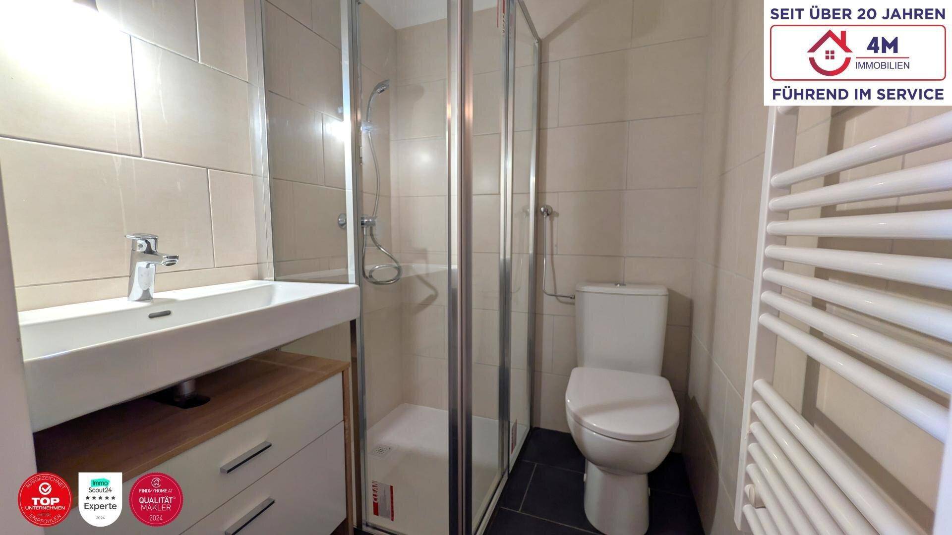 Modernes Badezimmer mit Duschkabine, Waschbecken, WC und beheiztem Handtuchhalter.
