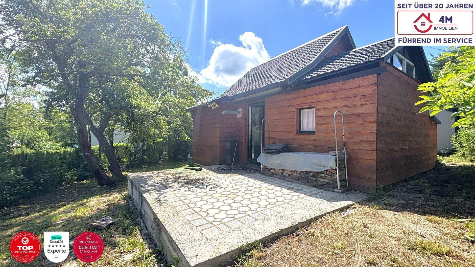 Gepflasterte Terrasse hinter dem Holzhaus, umgeben von Grün und Bäumen.