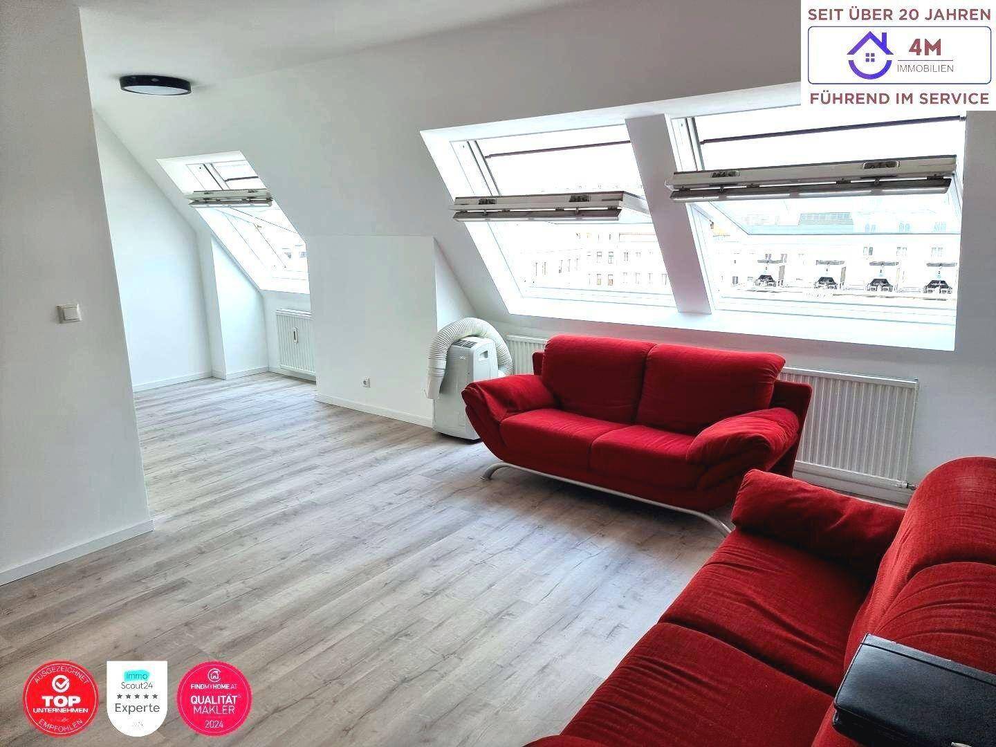 Helles Wohnzimmer im Dachgeschoss mit roten Sofas und großen Dachfenstern, die viel Licht hereinlassen.