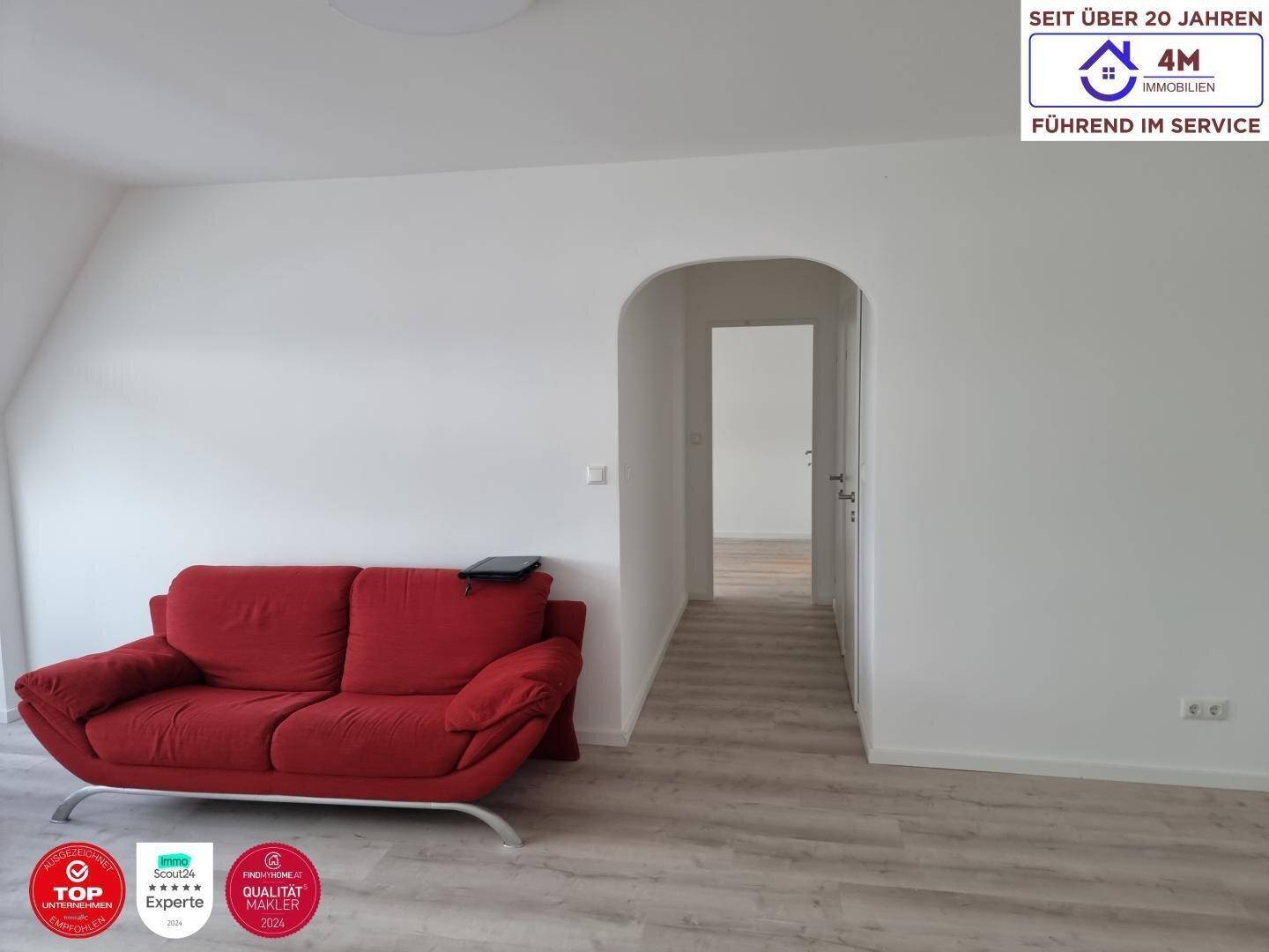 Gemütlicher Wohnbereich mit rotem Sofa und einem eleganten Rundbogen, der zu einem weiteren Raum führt.