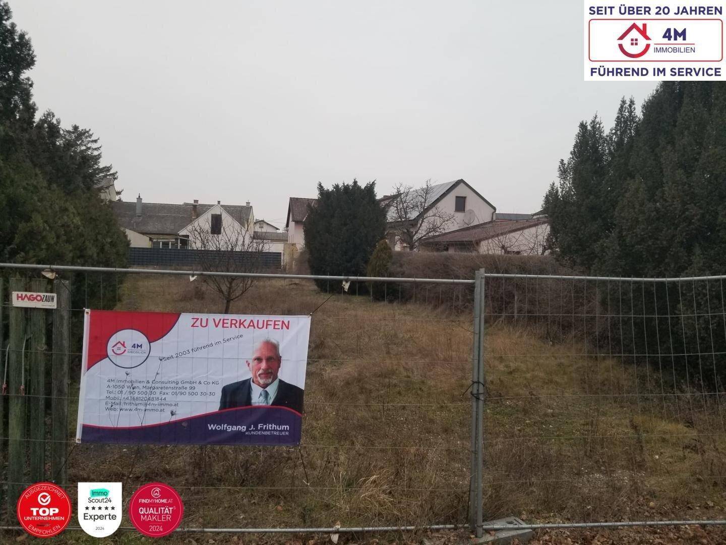 Grundstück mit 'Zu verkaufen'-Schild an einem Zaun und Blick auf die Nachbarschaft unter trübem Himmel.