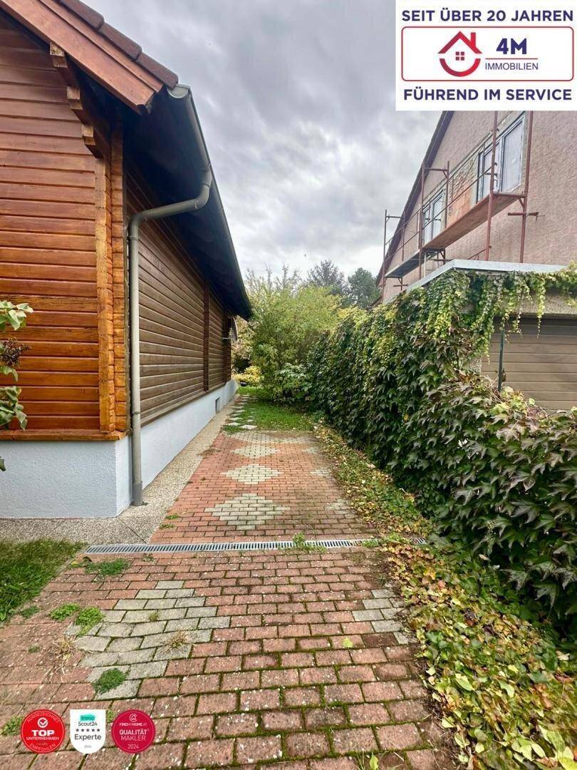 Gepflasterter Weg zwischen zwei Häusern, umgeben von üppigem Grün.
