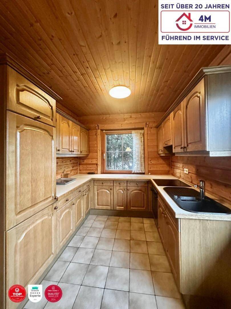 Funktionale Küche mit Holzschränken, Fliesenboden und Fenster mit Blick ins Grüne.