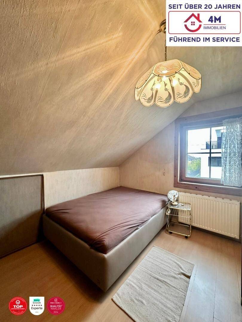 Schlafzimmer im Dachgeschoss mit schrägen Wänden, Fenster und einfacher Einrichtung.