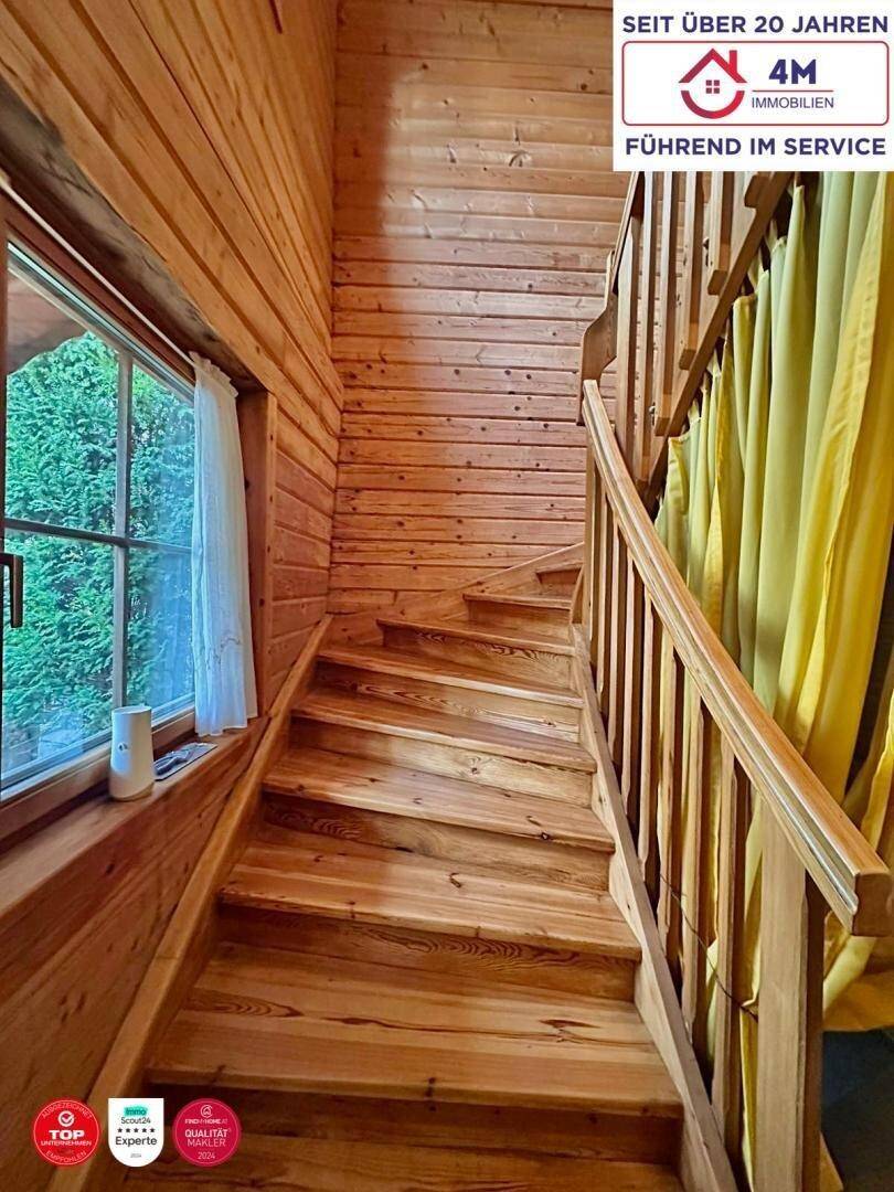 Holztreppe führt in die oberen Stockwerke, umgeben von Holzwänden und einem Fenster.