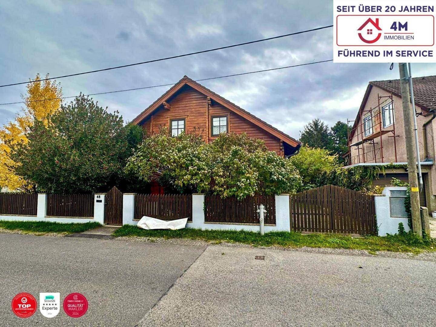 Ansicht des Holzhauses von der Straße mit Vorgarten und Nachbargebäude.