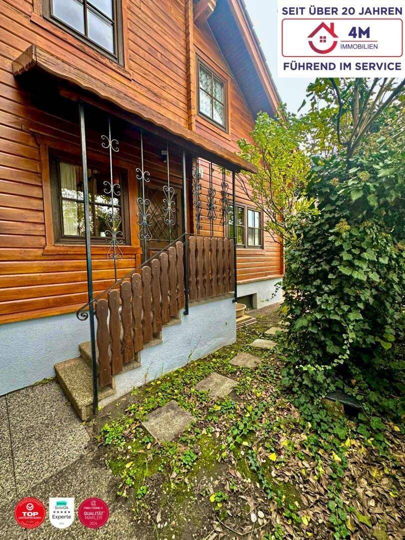 Eingangsbereich des Holzhauses mit überdachter Treppe und schmiedeeisernem Geländer.