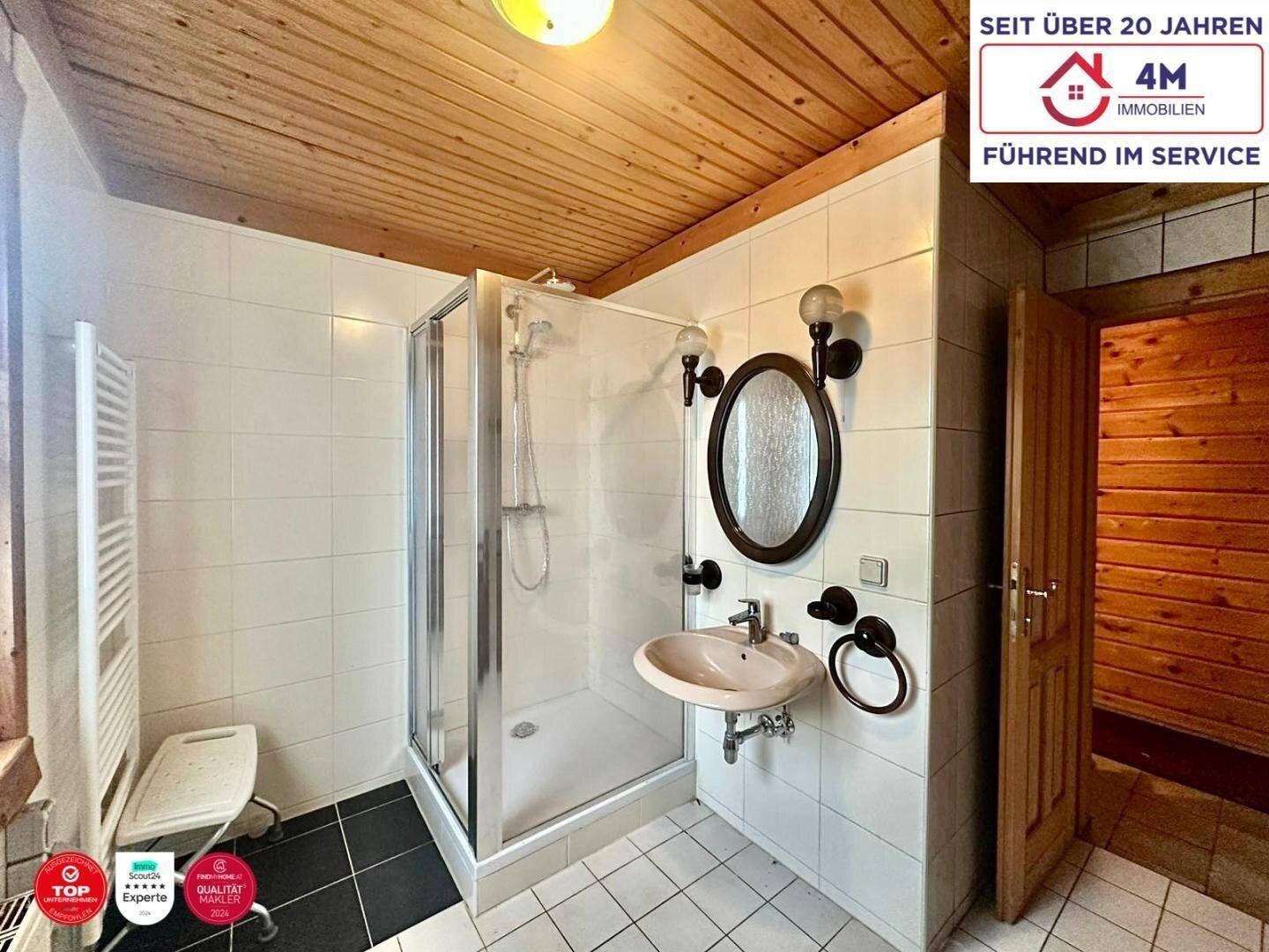 Badezimmer mit Duschkabine, Waschbecken und beheiztem Handtuchhalter, gefliest in Weiß.