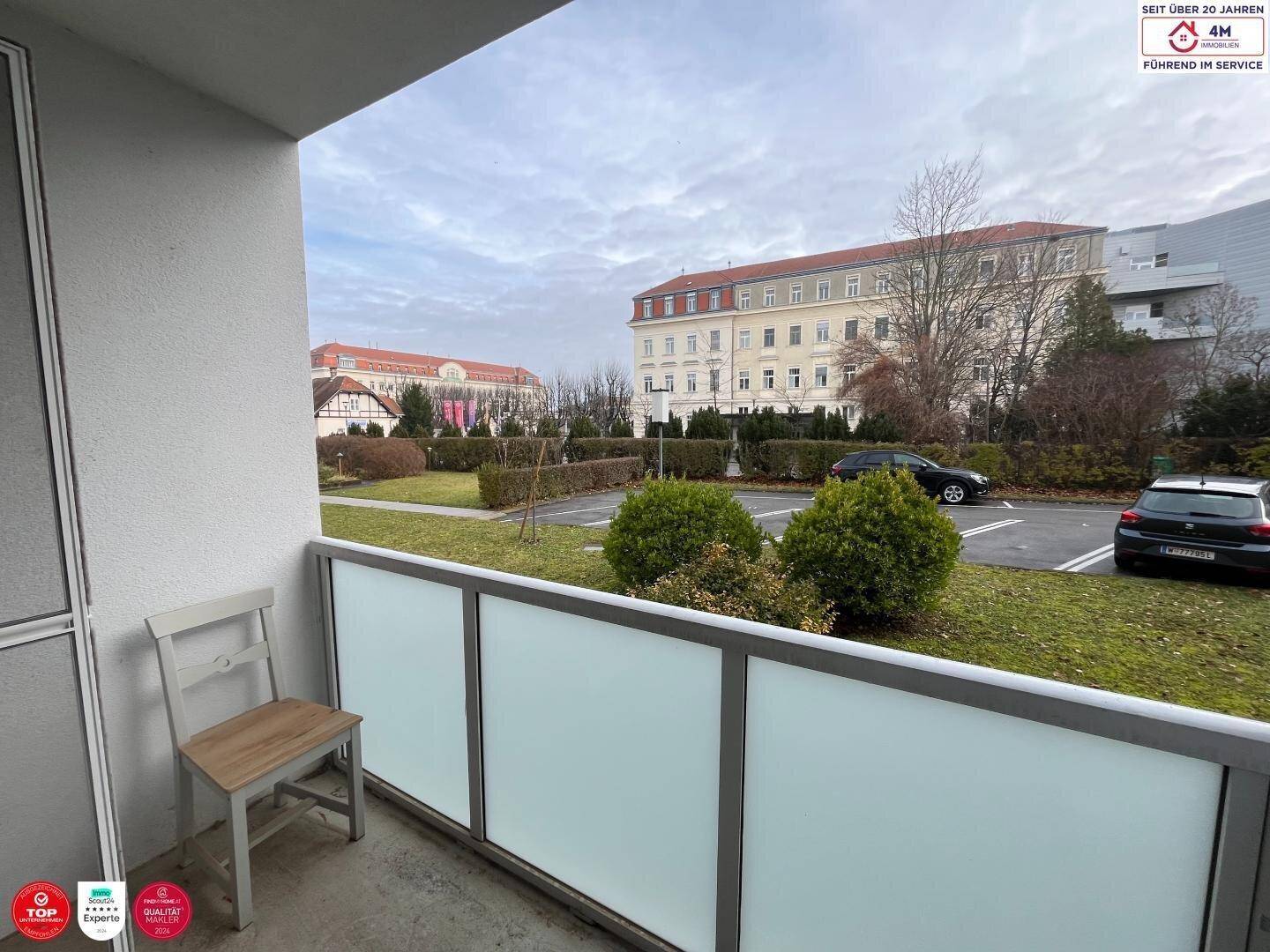 Balkon mit Blick auf einen begrünten Innenhof und umliegende Gebäude.