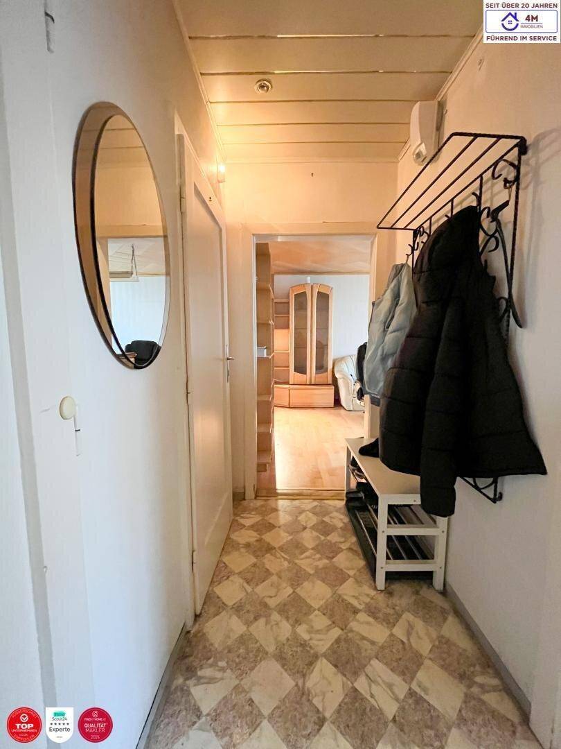 Schmaler Flur mit gemustertem Fliesenboden und Garderobe.