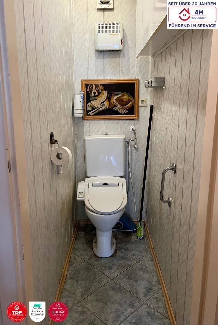 Kleines separates WC mit Wandfliesen, Toilette und Haltegriffen.