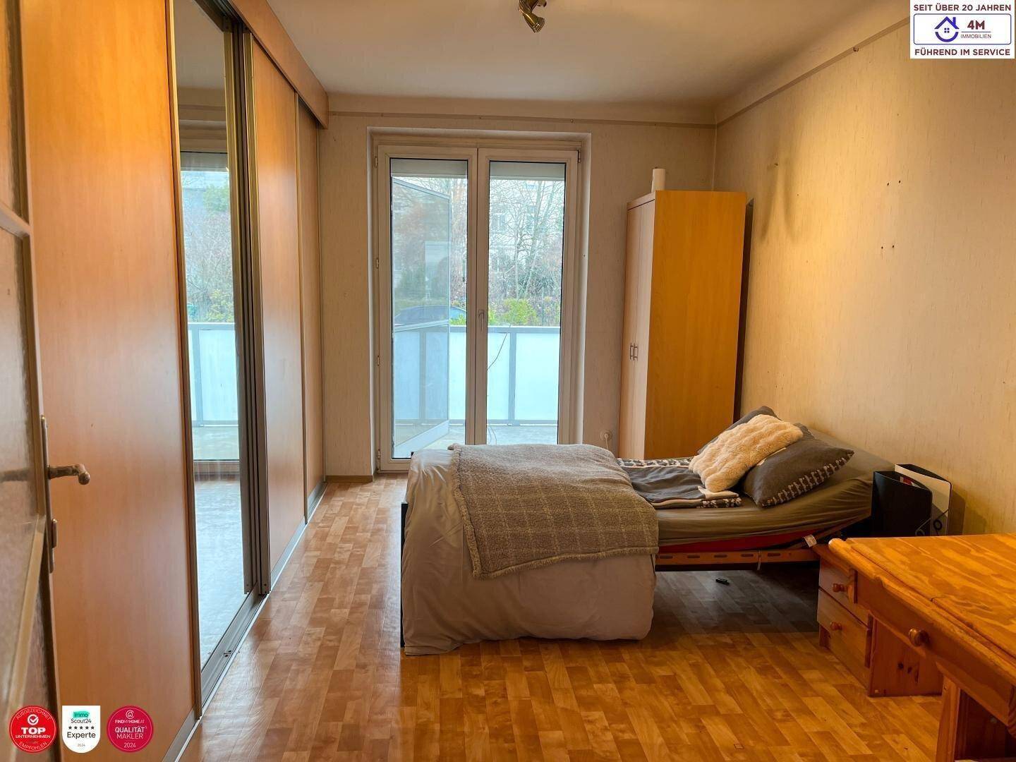 Schlafzimmer mit Laminatboden, Schiebetüren und Zugang zum Balkon.