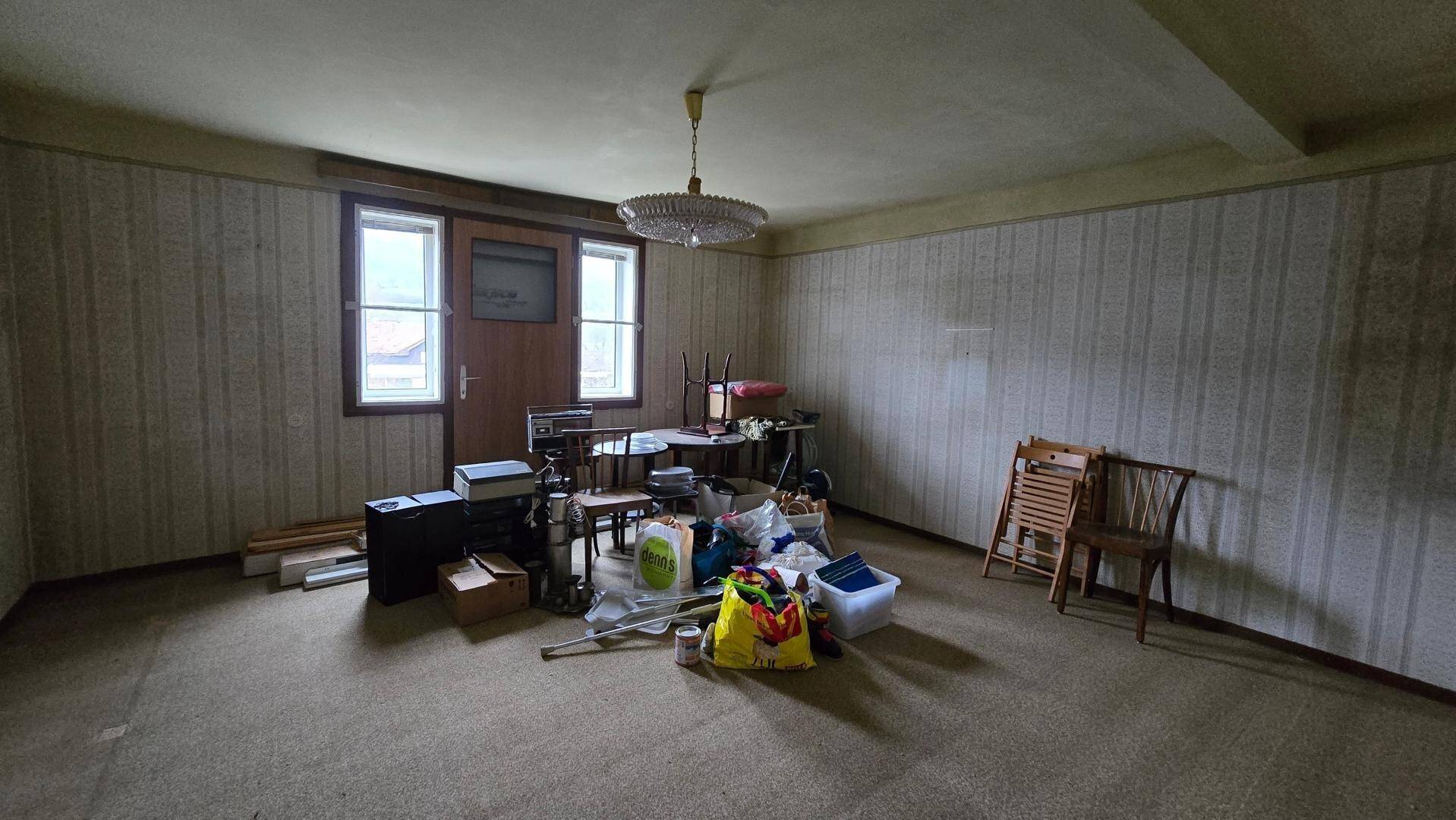 Geräumiges Zimmer mit Teppichboden und strukturierten Tapeten, derzeit als Abstellraum genutzt.