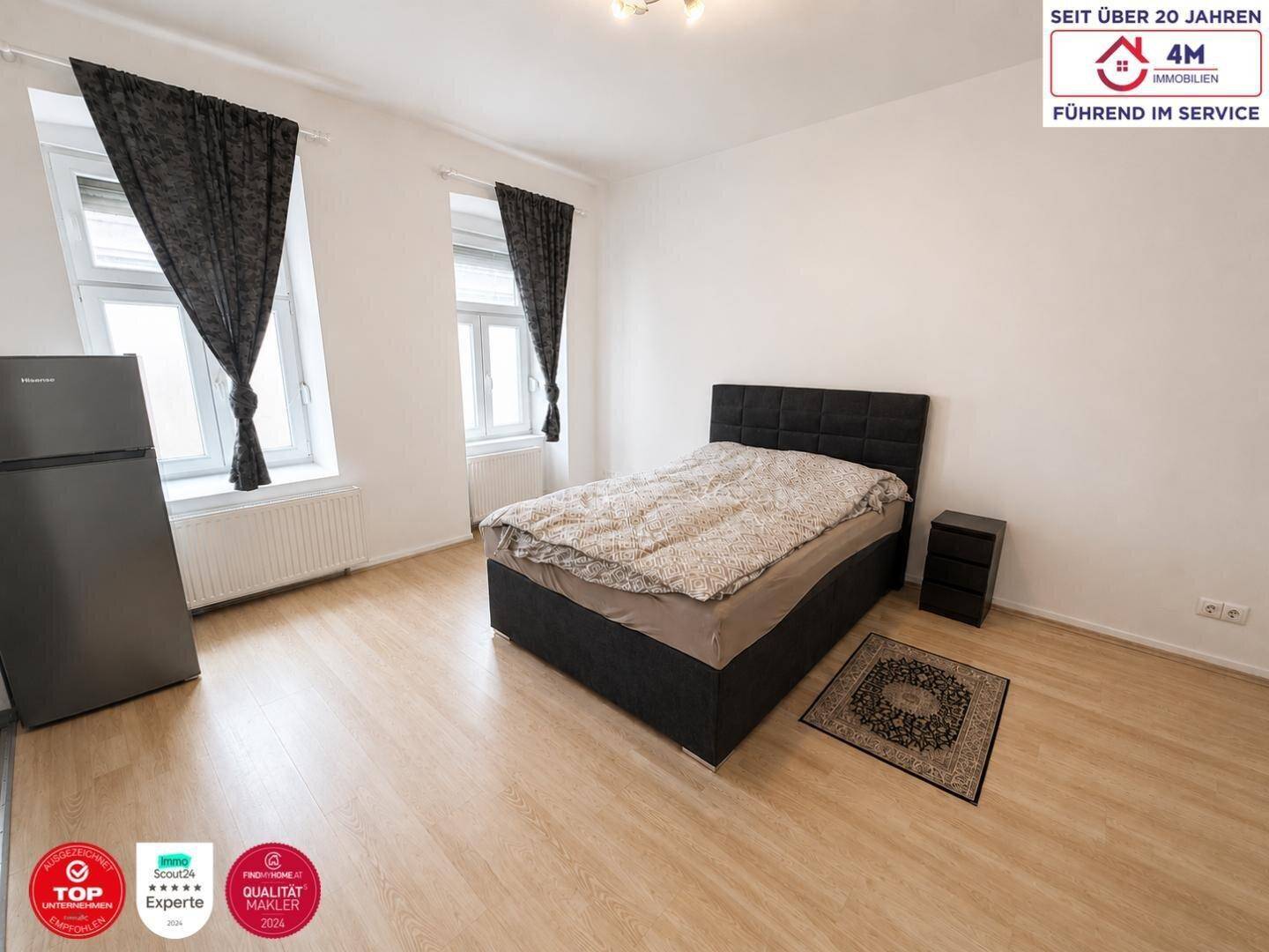 Helles Schlafzimmer mit Doppelbett, zwei Fenstern und dunklen Vorhängen, ausgestattet mit Laminatboden.