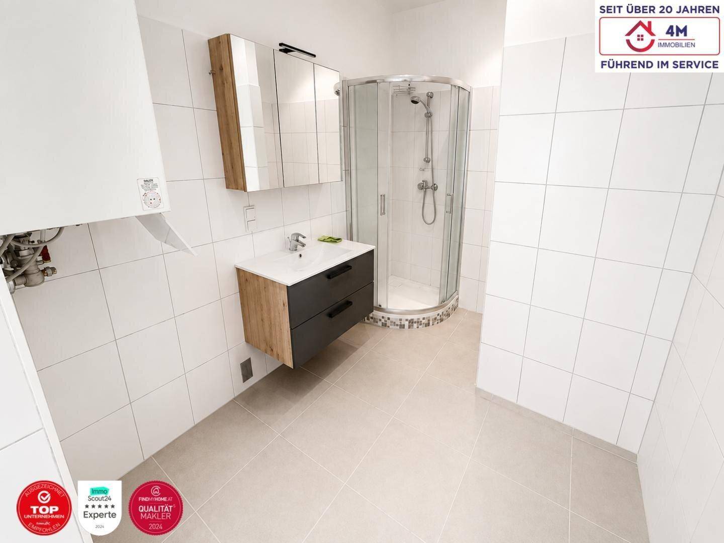 Modernes Badezimmer mit weißen Fliesen, Waschtisch, Spiegelschrank und einer runden Duschkabine.