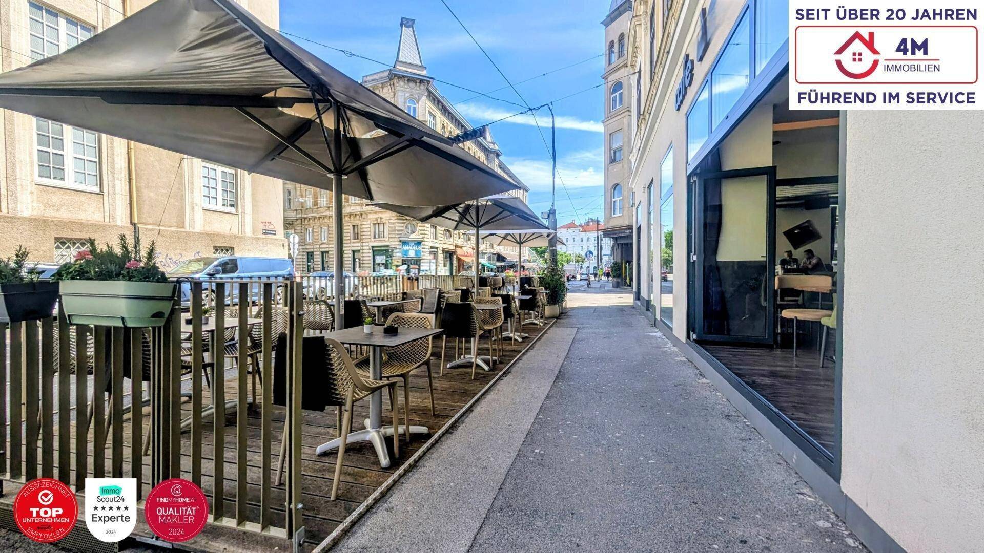 Belebte Straße mit Außenterrasse eines Cafés, Sonnenschirmen und angrenzenden Gebäuden.